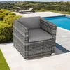An outdoor patio setting with a rattan armchair next to a swimming pool, with lounge chairs and a scenic landscape in the background. Produktbild-Vorschau