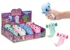 A display box of squishy axolotl toys, with a hand squeezing one and three individual toys shown separately. Produktbild-Vorschau