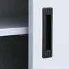 A close-up view of a black handle on a white cabinet door, with a shelf visible inside the cabinet. Produktbild-Vorschau