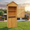 A wooden garden shed with its door open, standing on a grassy lawn with potted plants and outdoor furniture in the background. Produktbild-Vorschau