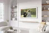 A modern living room with a Samsung Frame TV displaying artwork, a shelf with decorative items, and a sofa with cushions. Voir les images du produit