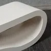 Close-up of a white curved cat scratching board on a dark wooden floor. Produktbild-Vorschau