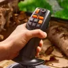 A hand holding a black and orange joystick controller in a natural, outdoor setting with blurred background. Anteprima dell’immagine prodotto