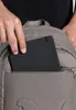 A person is putting a black notebook into the front pocket of a brown backpack. Anteprima dell’immagine prodotto