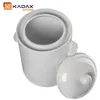 A white ceramic pot with its lid slightly ajar, set against a white background. A logo and text are visible in the top left corner. Podgląd zdjęcia produktu