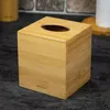 A bamboo tissue box sits on a dark countertop, with a blurred background of a brick wall and a roll of paper towels. Náhled obrázku produktu
