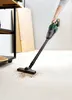 A person is using a cordless handheld vacuum cleaner to clean up debris on a light-colored floor in what appears to be a workshop or garage setting. Produktbild-Vorschau