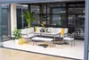 A modern outdoor lounge and dining set arranged on a patio with large glass windows in the background. Produktbild-Vorschau