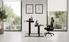 Two standing desks are set up in a modern office space with large windows and artwork on the wall. An ergonomic chair is next to one of the desks. Anteprima dell’immagine prodotto