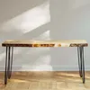 A live-edge wooden table with black hairpin legs against a light gray wall with sunlight casting shadows. Podgląd zdjęcia produktu