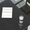A close-up view of a glass table with a glass of ice water and a white object on it. Produktbild-Vorschau