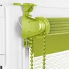Close-up of a green roller blind mechanism attached to a white window frame. Produktbild-Vorschau