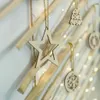 Close-up of wooden Christmas tree decorations hanging on branches, with blurred fairy lights in the background. Podgląd zdjęcia produktu