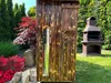A wooden smoker with a silver cylinder attached, set in a garden with a barbecue grill in the background. Anteprima dell’immagine prodotto