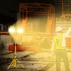 A construction worker in a safety vest points towards a construction site illuminated by a bright LED work light. Náhľad obrázku produktu