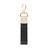 A close-up studio shot of a black and gold keychain with a beige leather accent. Produktbild-Vorschau