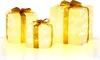 Three illuminated gift boxes with gold ribbons and bows, displayed on a white surface with a yellow glow underneath. Podgląd zdjęcia produktu