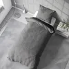 A neatly made bed with grey bedding in a room with natural light casting shadows. Produktbild-Vorschau