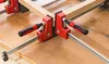 Two clamps are holding together wooden pieces at a right angle on a wooden surface. Náhľad obrázku produktu