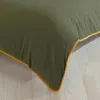A close-up view of the corner of a green duvet cover with a yellow trim, lying on a light-colored wooden floor. Produktbild-Vorschau