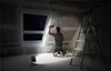A person is working on a wall near a window, illuminated by a portable LED spotlight. Produktbild-Vorschau