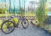 An electric bicycle is parked on a gravel path in front of a mural depicting a forest and a train. Produktbild-Vorschau