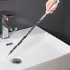 A hand is using a long, flexible brush to clean a sink drain. Produktbild-Vorschau