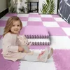 Kleinkind sitzt auf einer rosa-weißen ineinandergreifenden Schaumstoff-Spielmatte und hält ein Stofftier-Häschen Anteprima dell’immagine prodotto