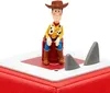 A close-up view of a Woody toy figure from Toy Story sitting on a red box with two gray shark fins protruding from a white surface in front of him. Produktbild-Vorschau