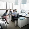 Three people are in a modern office setting, gathered around a desk and discussing documents. Podgląd zdjęcia produktu