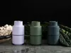 Three grinders in different colors are displayed on a textured surface with mushrooms and kale in the background. Produktbild-Vorschau