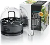 An electric egg cooker with a transparent lid and a measuring cup, next to its product packaging which shows images of cooked eggs and spinach. Produktbild-Vorschau