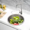 A kitchen sink filled with fresh vegetables, with a faucet and a jar of pasta in the background. Náhled obrázku produktu