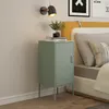 A mint green nightstand with a locked door and slatted ventilation is placed next to a bed with yellow and white bedding. A wall lamp with a black shade and gold accents is mounted on the wall above the nightstand. Books and a small potted plant are on top Anteprima dell’immagine prodotto