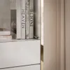 A close-up view of books on a shelf above white drawers, with a curtain in the background. Produktbild-Vorschau