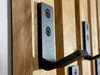 A close-up shot of black metal coat hooks mounted on a wooden panel wall. Náhled obrázku produktu