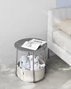 A round side table with a storage basket filled with stuffed toys next to a bed. Náhled obrázku produktu