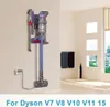 A wall-mounted docking station for a Dyson vacuum cleaner, with various attachments stored on it. The scene is set in a clean, modern room with a window and towels on a rack. Produktbild-Vorschau