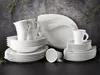 A collection of white porcelain dinnerware, including plates, bowls, and cups, arranged on a dark surface against a textured gray background. Produktbild-Vorschau