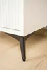 Close-up of the bottom corner of a white cabinet with fluted detailing on the left, resting on three black angled legs. Produktbild-Vorschau