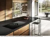 A modern kitchen island with an integrated induction cooktop and downdraft ventilation, set in a spacious, open-plan living area with large windows overlooking a garden. Náhled obrázku produktu