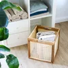 A storage basket with towels is placed on a wooden floor next to a white shelving unit with folded towels and blankets. Produktbild-Vorschau