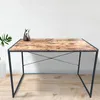 A desk with a wooden top and black metal legs, set against a white tiled wall and wooden floor. Produktbild-Vorschau