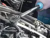 A person's hand wearing a glove is using a torque wrench to tighten a bolt on a car engine. Náhľad obrázku produktu