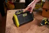 A hand is shown pressing a button on a Ryobi speaker, which is placed on a wooden surface next to a drill and screws. Anteprima dell’immagine prodotto