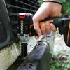 A person is using a cordless impact wrench to tighten a bolt on a weathered metal surface, possibly a vehicle bumper or frame, outdoors. Podgląd zdjęcia produktu