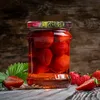 A jar of strawberries in syrup with some fresh strawberries and a leaf on a wooden surface. Voir les images du produit