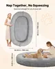 A woman is standing next to a large oval pet bed, and a dog is lying in a similar pet bed with a woman petting it. Dimensions are shown. Voir les images du produit