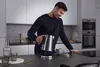 A man is pouring hot water from a kettle into a mug in a modern kitchen. Anteprima dell’immagine prodotto