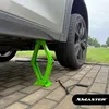 A green scissor jack is lifting a car, with a tire iron on the ground next to it. Produktbild-Vorschau